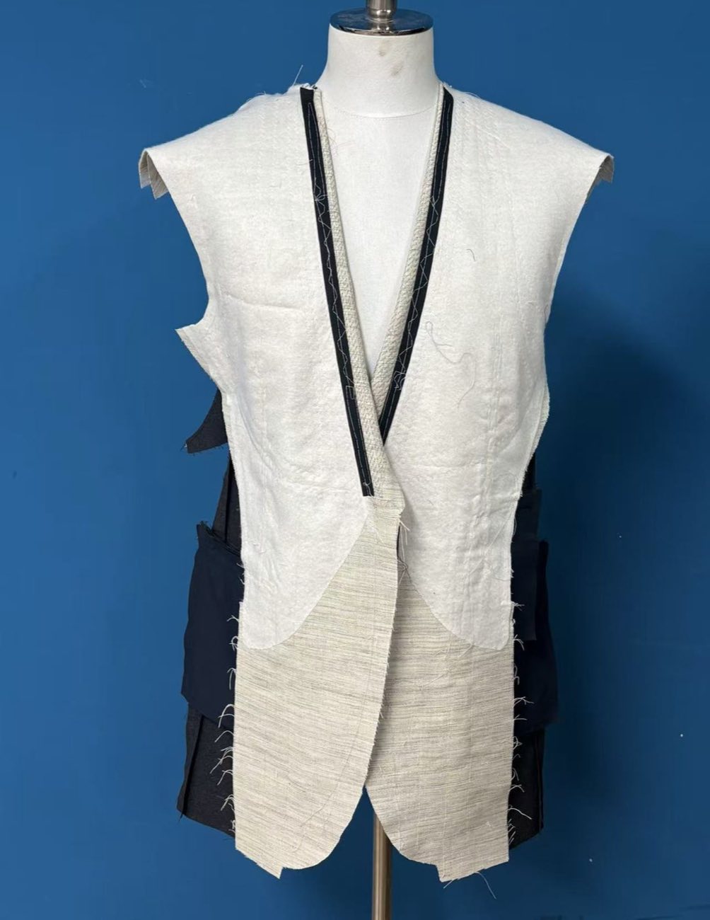 A navy jacket on a dress form during making, with a full length canvas basted across the front