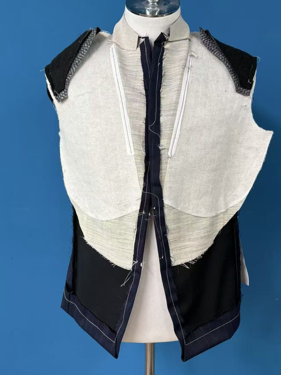 A navy jacket front on a dress form during making, opened to show the half canvas and chest piece before lining