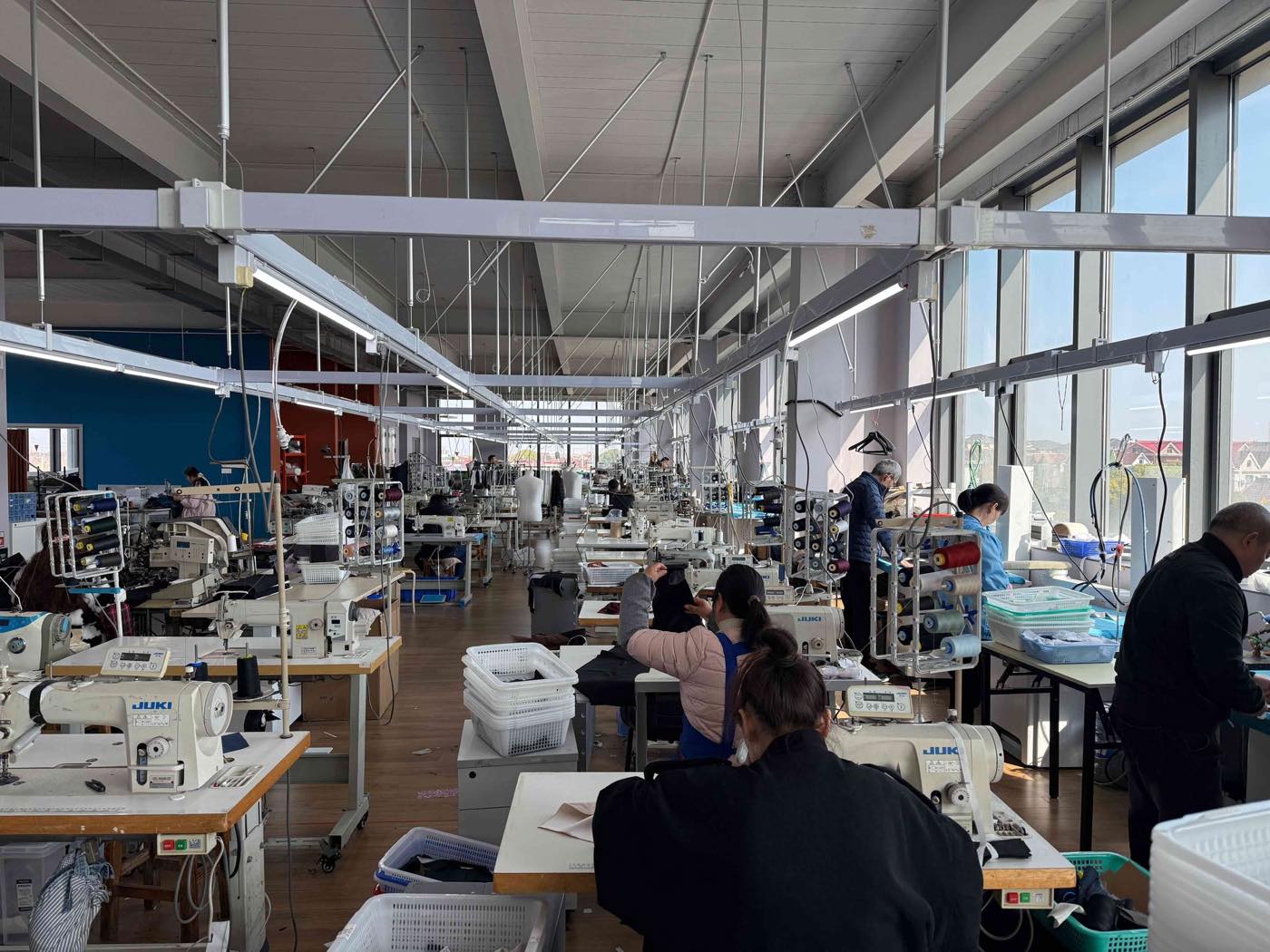The sewing floor of the Shanghai workshop, with machinists at rows of stations under long strip lights